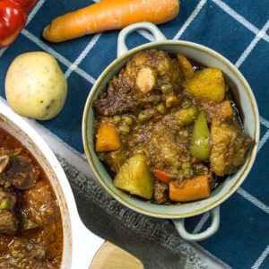stew in a bowl on top of table with vegetables in the side