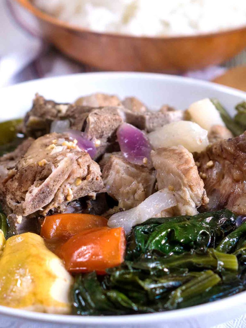 pork stew in a bowl with vegetables on top of table