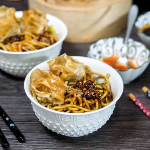 noodles in a bowl with sauce and toppings on top of table with chopsticks at the sides