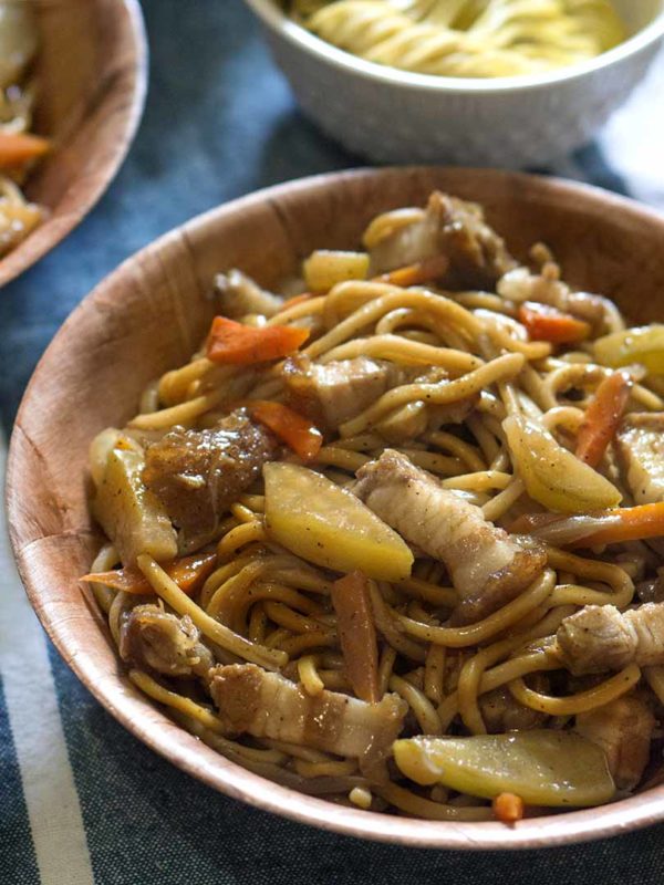 noodles with pork and carrots in a bowl on top of table
