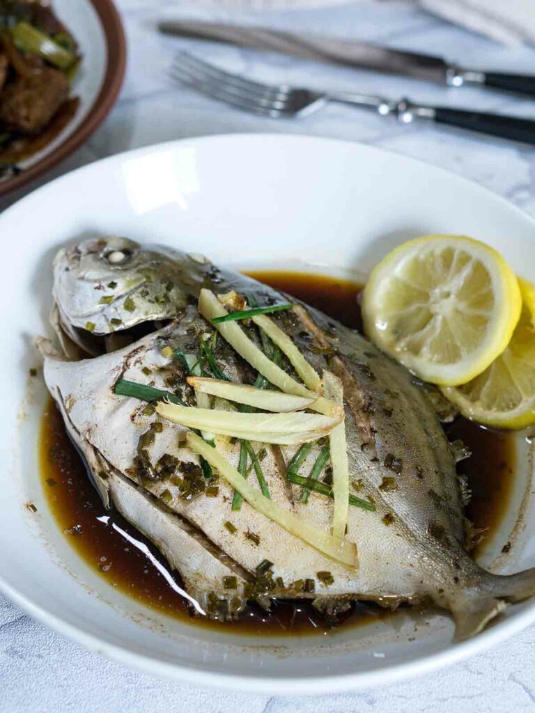 cooked fish in sauce with ginger and lemon in a plate